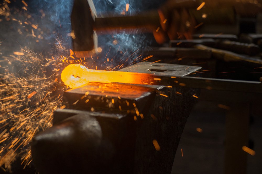 Een smid slaat met de hamer op gloeiend ijzer op het aambeeld in de werkplaats in Baflo
