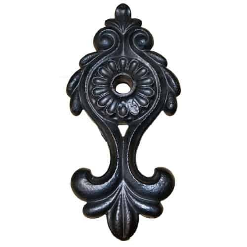 Zwart gietijzeren muurankerrozet met een sierlijk ontwerp, voorzien van een centraal bloemmotief, krullen en een gat in het midden.