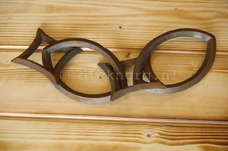 Gietijzeren sierketting bestaande uit drie in elkaar grijpende schakels, elk in de vorm van een gestileerde vis, liggend op een houten ondergrond.