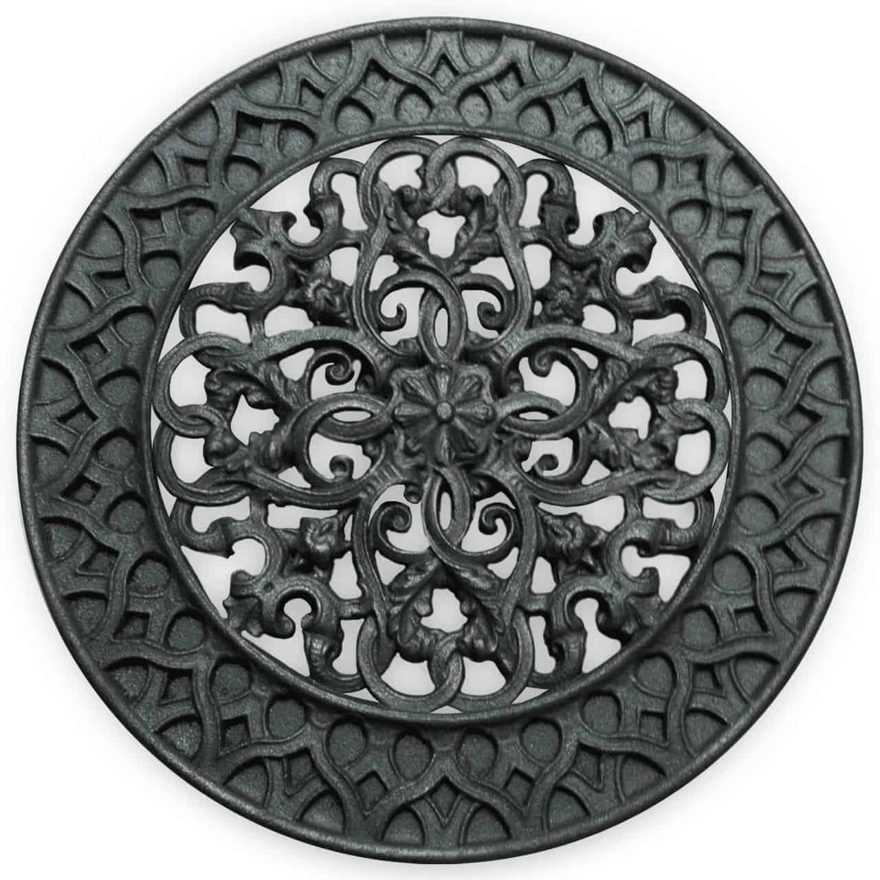 Rond gietijzeren ventilatorrooster met een gedetailleerd floraal en sierlijk ontwerp in het midden, omringd door een decoratieve rand, afgebeeld tegen een witte achtergrond.