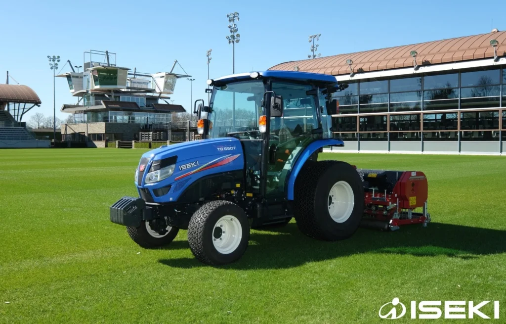 Iseki TG 6507 met cabine en een rode machine achterop op een grasveld bij een tribune