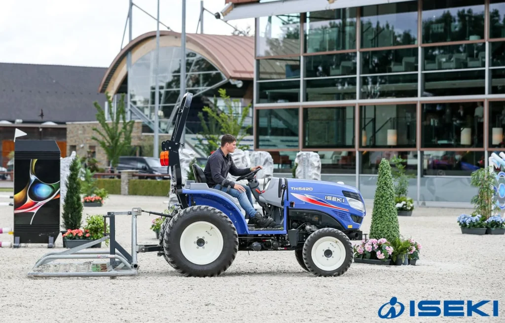 Iseki TH 5420 met veiligheidsbeugel en een werktuig achterop op een zandbaan bij een gebouw