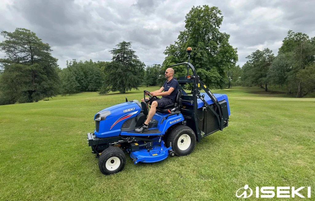 Bestuurder rijdt met de Iseki SXG 327 met opvangbak over een grasveld met bomen