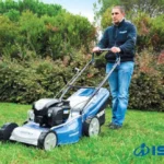 Man maait een gazon met de Iseki loopmaaier, struiken op de achtergrond
