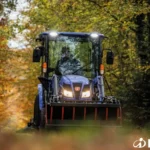 Iseki TH 5370 met cabine en frontlader, van voren gezien met koplampen aan op een bospad