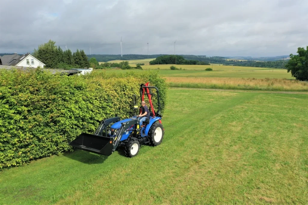 Iseki TLE 3410 met frontlader naast een heg, met een heggenschaar op een arm