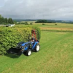 Iseki TLE 3410 met frontlader naast een heg, met een heggenschaar op een arm