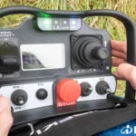 Twee handen houden de afstandsbediening met joystick en stopknop vast