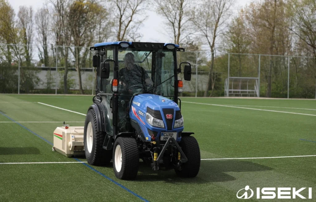 Iseki TH 5420 met cabine en een machine achterop op een sportveld