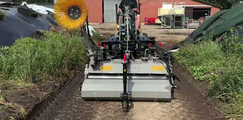 Jansen veegmachine uit de JK-serie met gele zijborstel aan een compacte lader op een erfpad