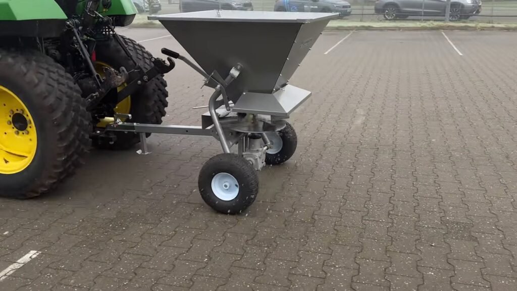 Jansen strooiwagen SW-200 achter een compacte trekker, strooimiddel op de bestrating