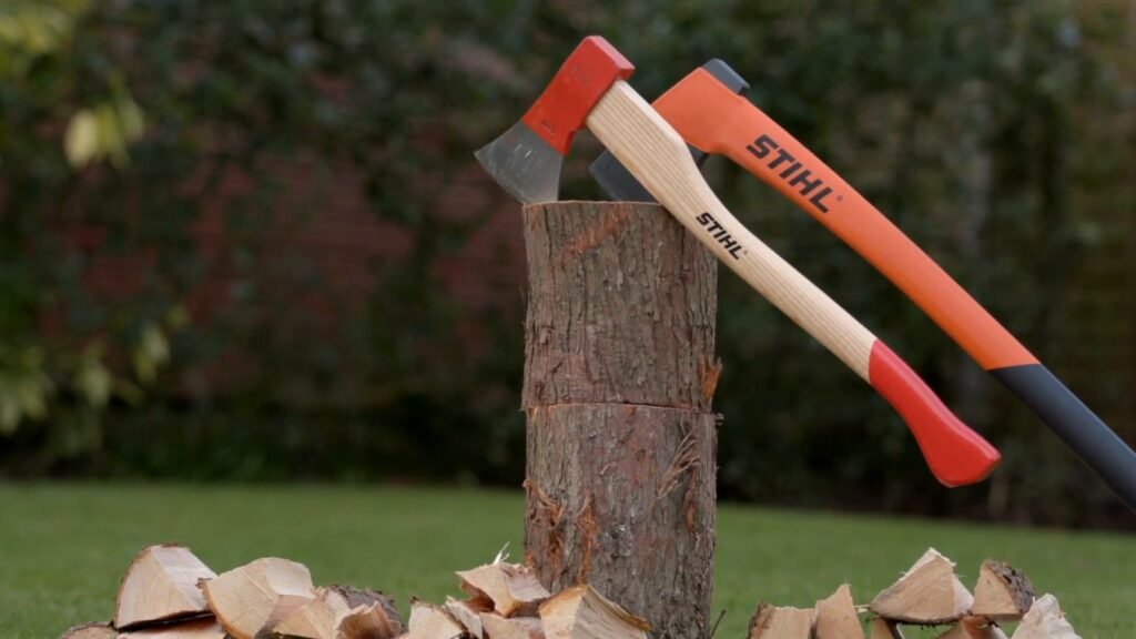 Een STIHL handbijl met houten steel en een bijl met langere kunststof steel in een hakblok