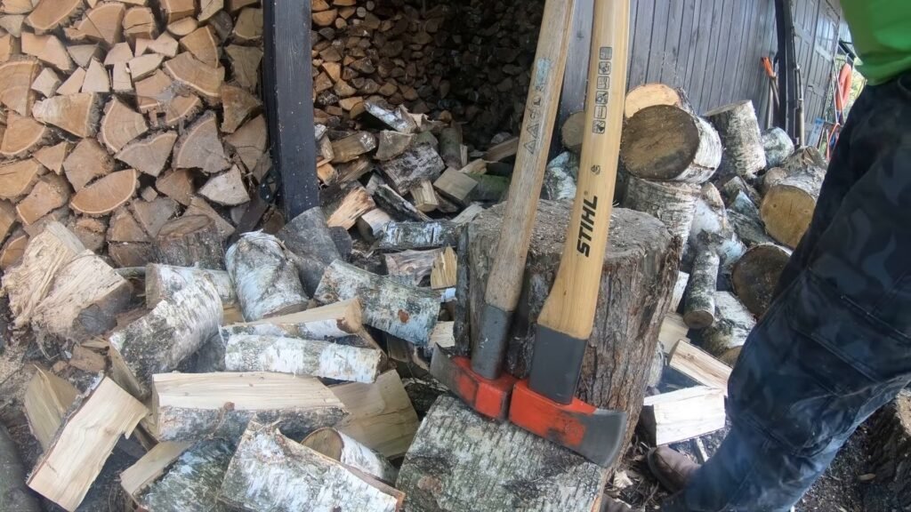 Twee STIHL bijlen met houten steel en rode kop tegen een hakblok naast een stapel brandhout