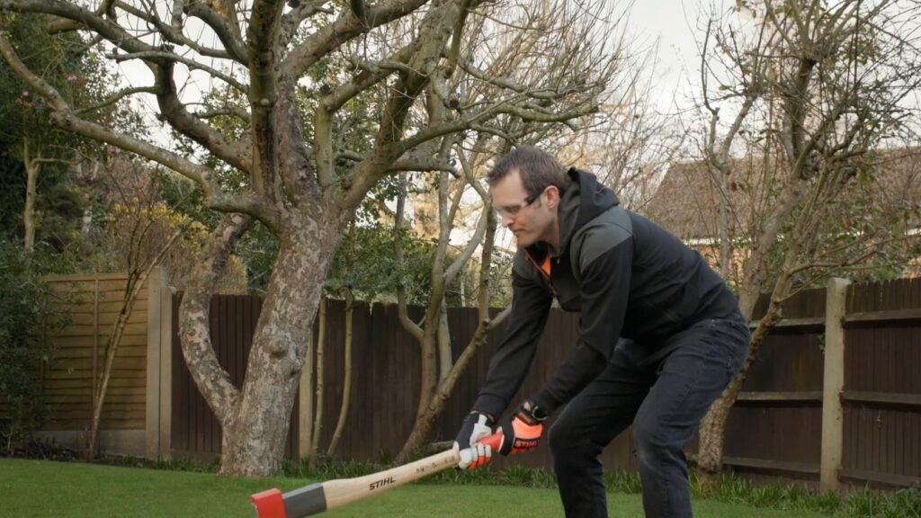 Man zwaait met een zware STIHL bijl met lange houten steel naar een blok in de tuin