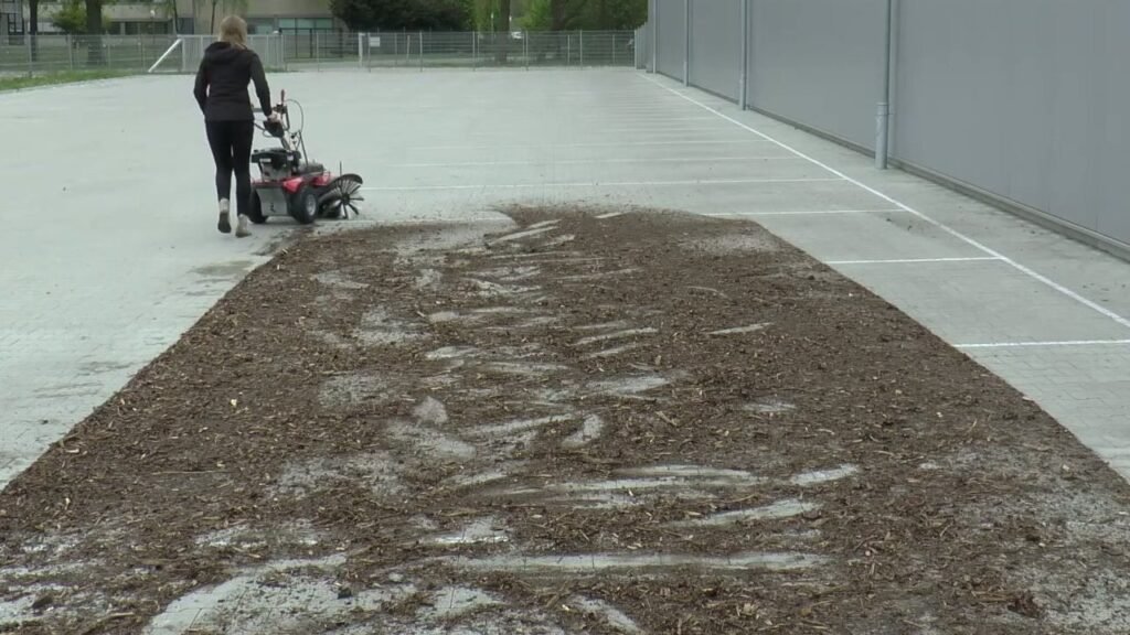 Veegmachine kiezen: een loopmachine met benzinemotor veegt een berg houtsnippers van een groot verhard terrein