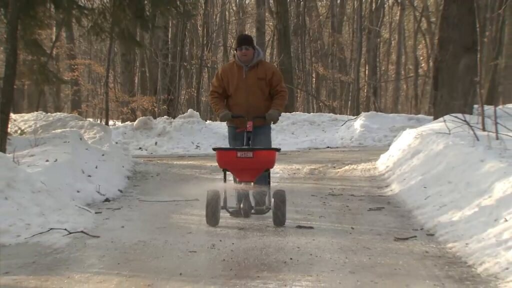 Duwstrooier van Western op een geruimd pad tussen twee wallen van weggeschoven sneeuw